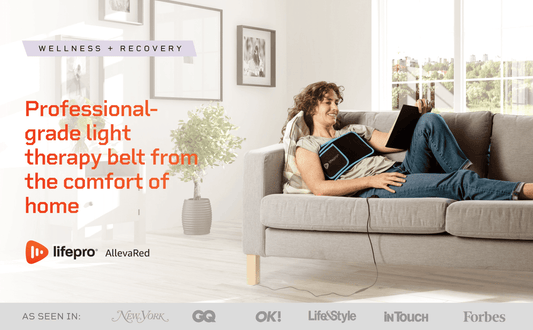 a woman wearing a red light therapy belt AllevaRed from Lifepro while relaxing on her sofa with a book