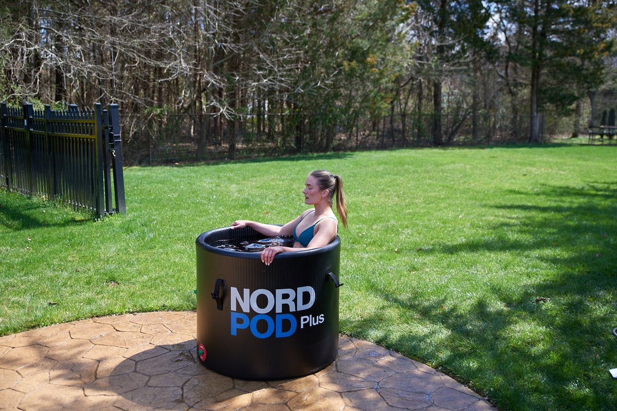 A woman relaxing in a cold plunge ice tub in an outdoor backyard lawn.