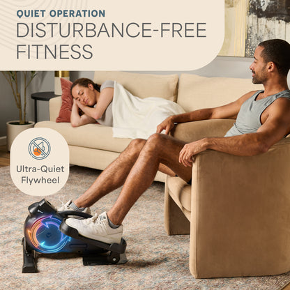 Woman asleep on a couch while a man sits nearby with his foot resting on the FlexStride elliptical's glowing blue flywheel, captioned 'Quiet Operation: Disturbance-Free Fitness — Ultra-Quiet Flywheel.'