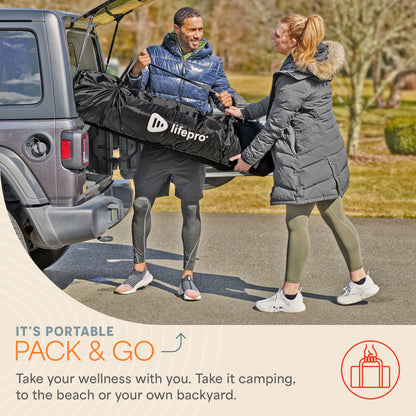 Man and woman carrying the folded ZenZone sauna tent in its LifePro-branded carry bag from a car trunk, captioned 'It's Portable: Pack & Go — Take your wellness with you. Take it camping, to the beach or your own backyard.'