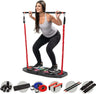 Woman doing a squat while pulling on the InfinityBox's resistance-band bar, with the folding base and its push-up handles, ab wheel, bands, and straps shown below.